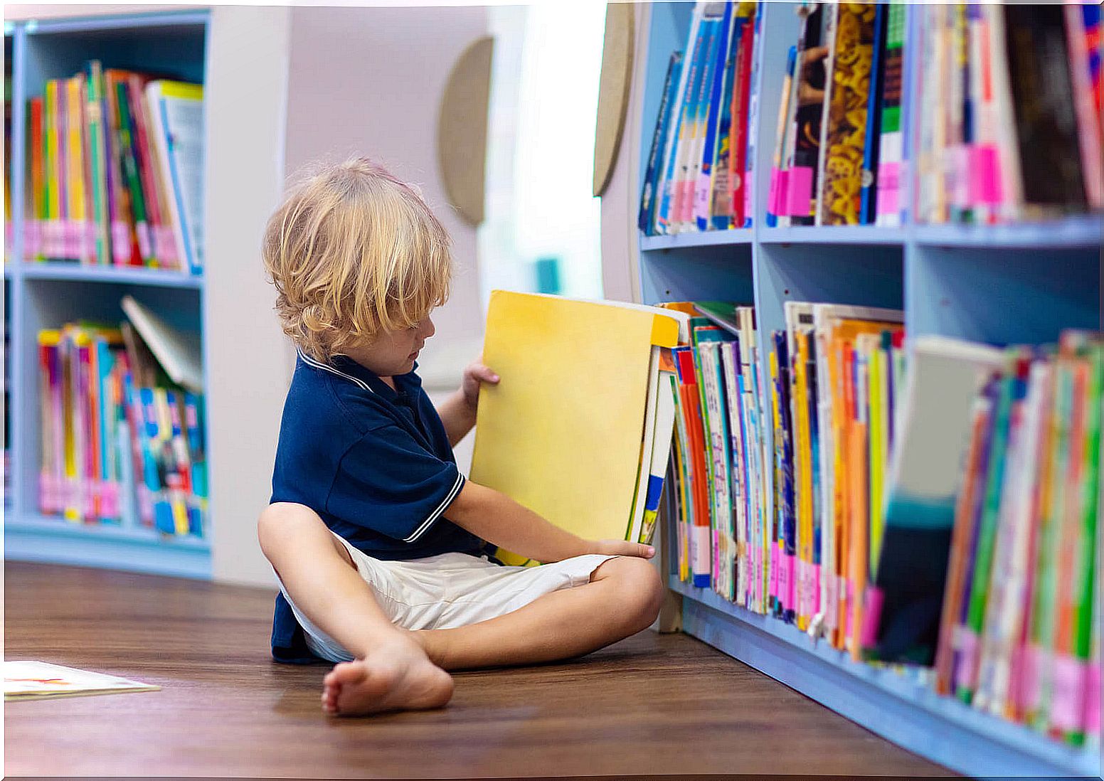 Boy picking up a book and reading in the classroom library.