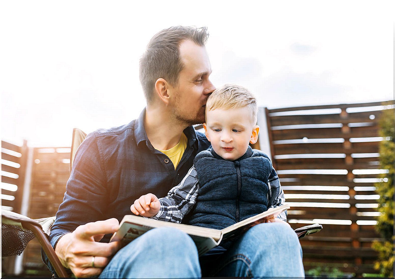 Father giving his son a kiss on the head while they read a haiku book.